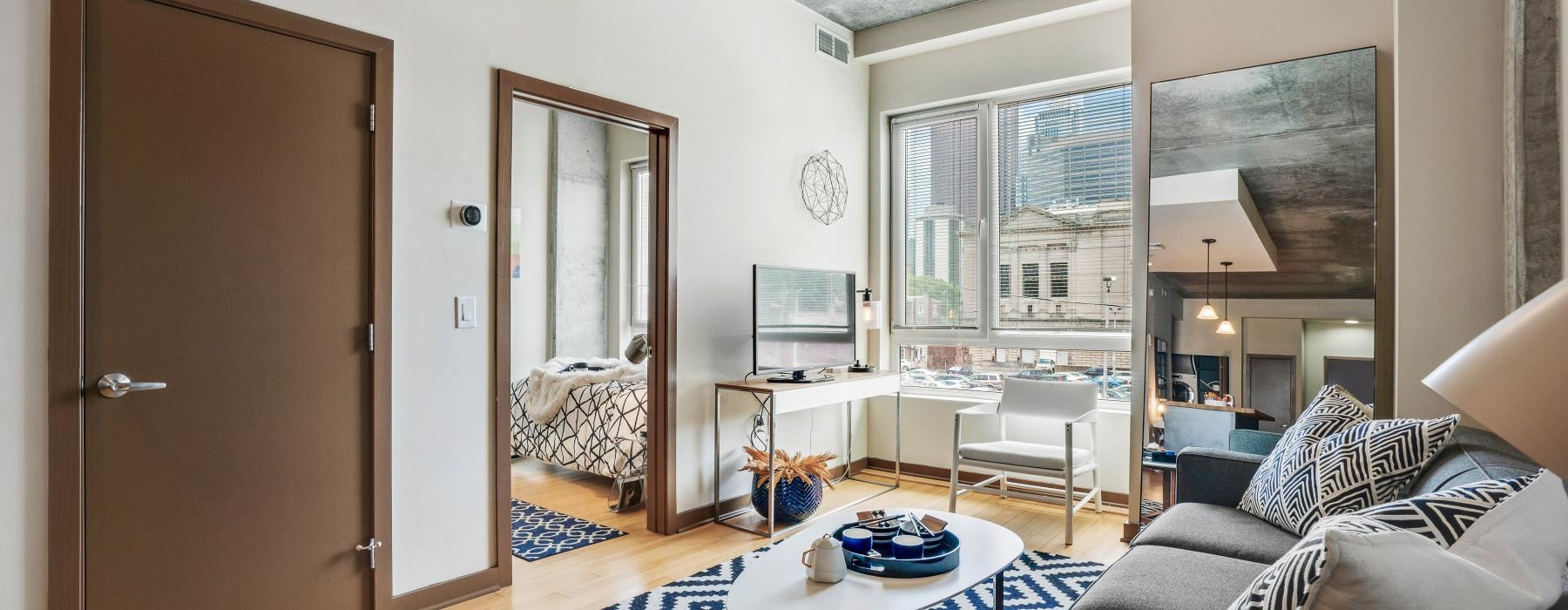 Living area with large window and view into bedroom at The Granary apartments in Central Philadelphia